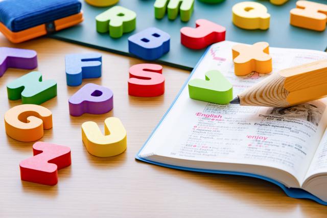 An image of an exercise book, a pencil and some colourful letters